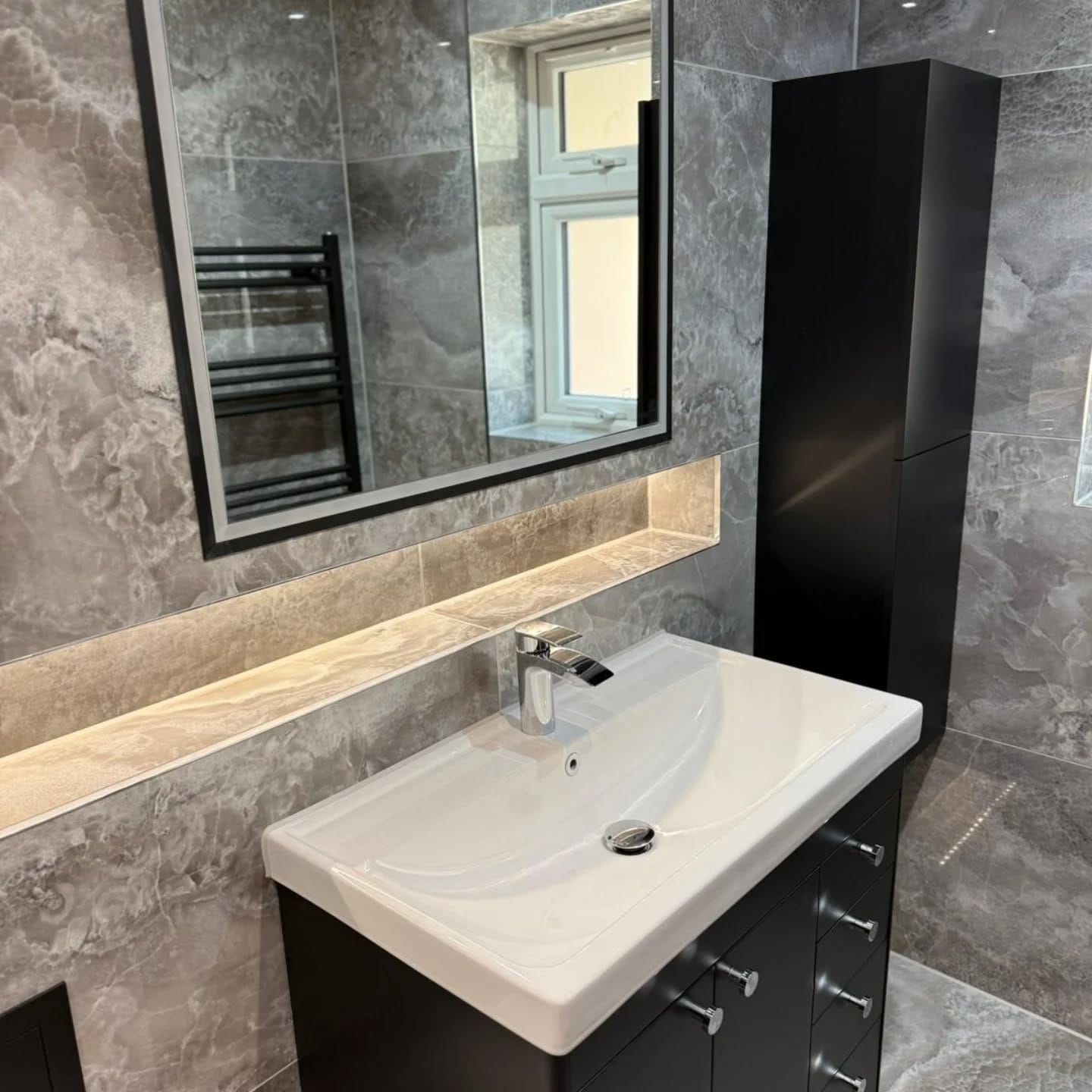 A spotless bathroom with marble-effect tiles and a dark vanity unit